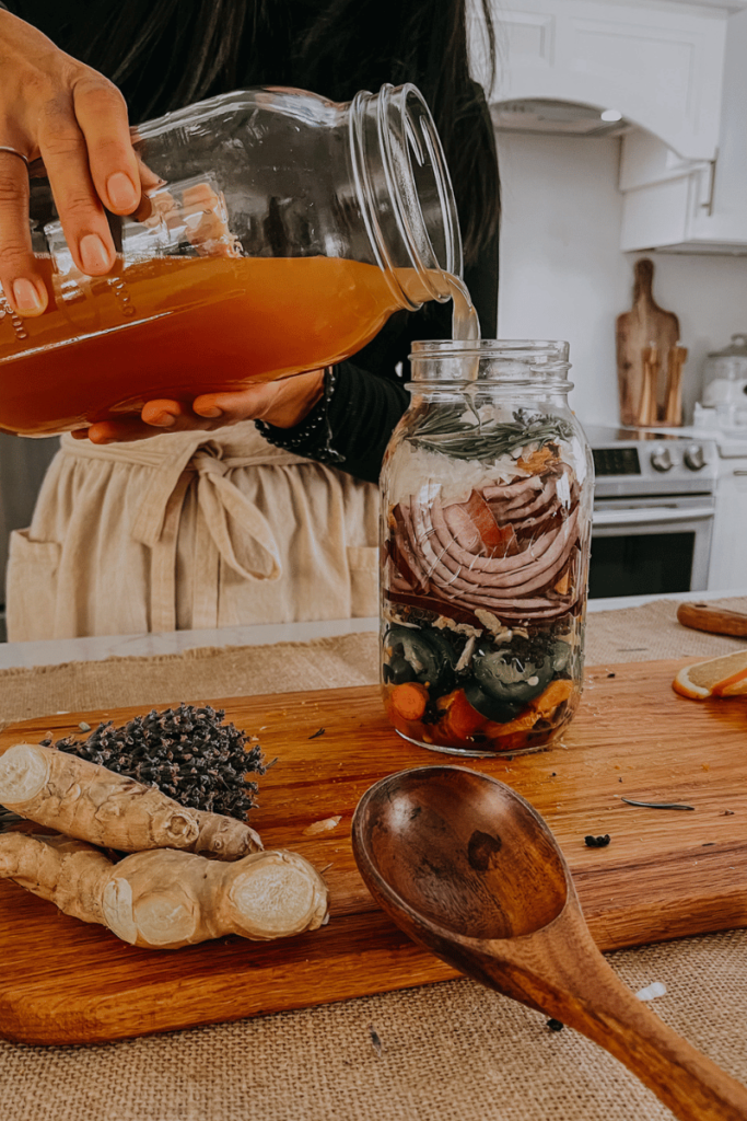 woman pouring apple cider vinegar into mason jar to make fire cider
