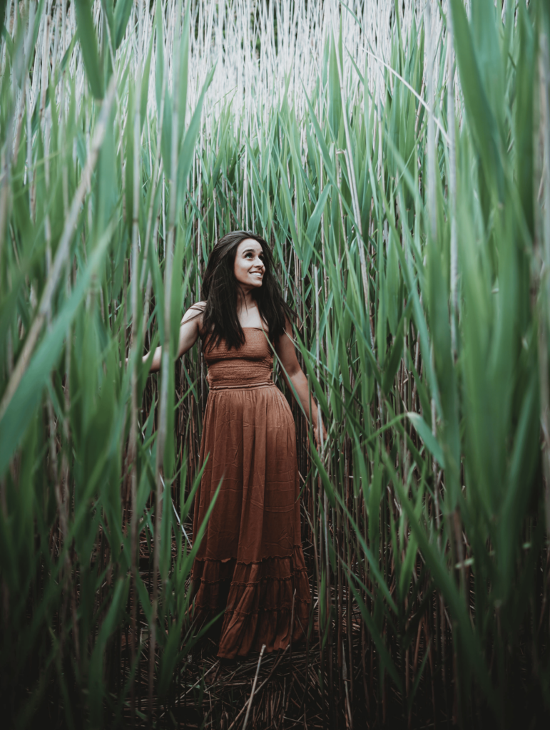 woman in long brown dress standing amidst tall reeds